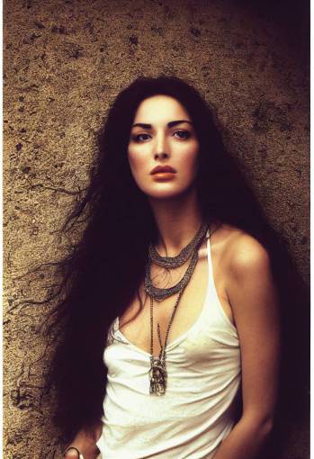 young Monica Bellucci at a hippie festival with touselled hair, light make up, small silver necklace, sheer white camisole, diffuse morning light, white textured wall, photo by Paolo Eleuteri Serpieri, Luis Royo, Paolo Roversi, 120mm lens,
