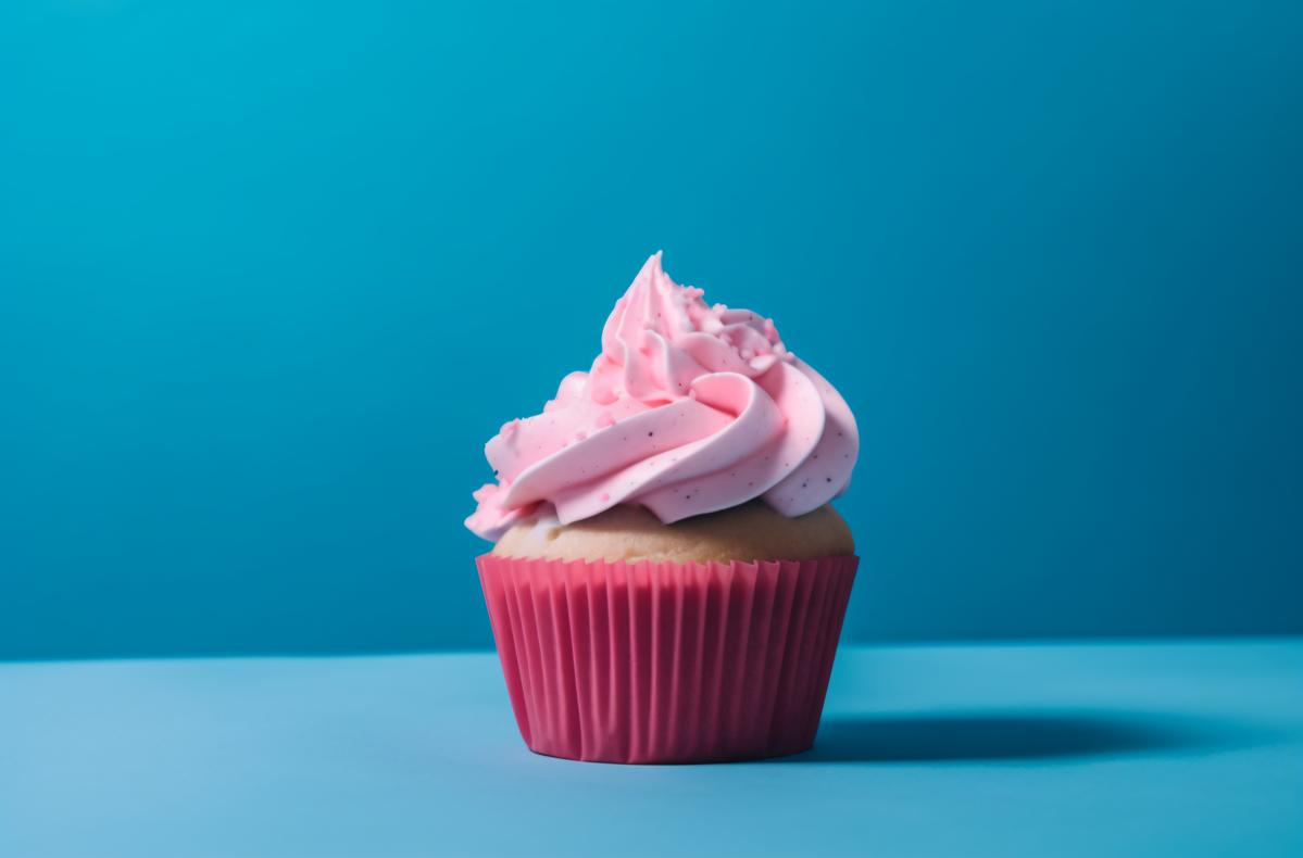 a pink frosted cupcake sits on a blue background picture